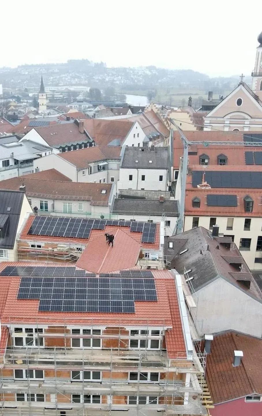 Dach eines Mehrfamilienhauses im Stadtzentrum von Cham mit zwei Photovoltaikanlagen in Ost-West-Ausrichtung, ein Monteur bei der Arbeit